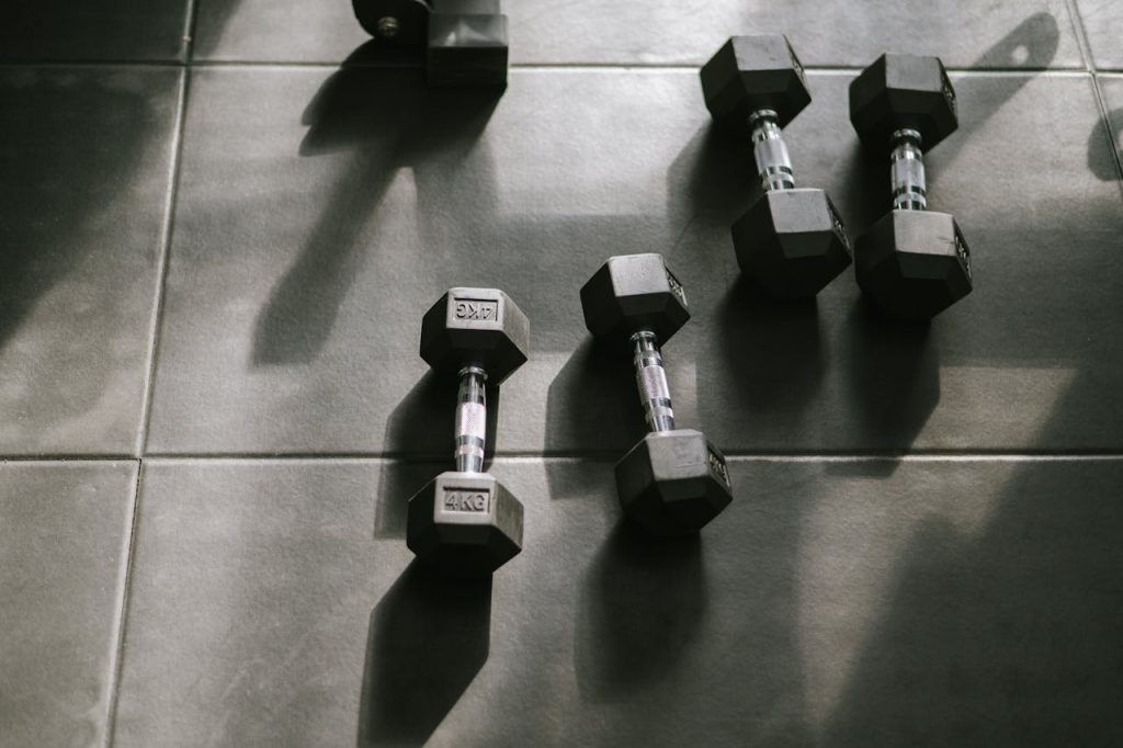 pexels-photo-16513597 Hexagonal dumbbells on a gym floor bathed in natural sunlight, creating dynamic shadows.